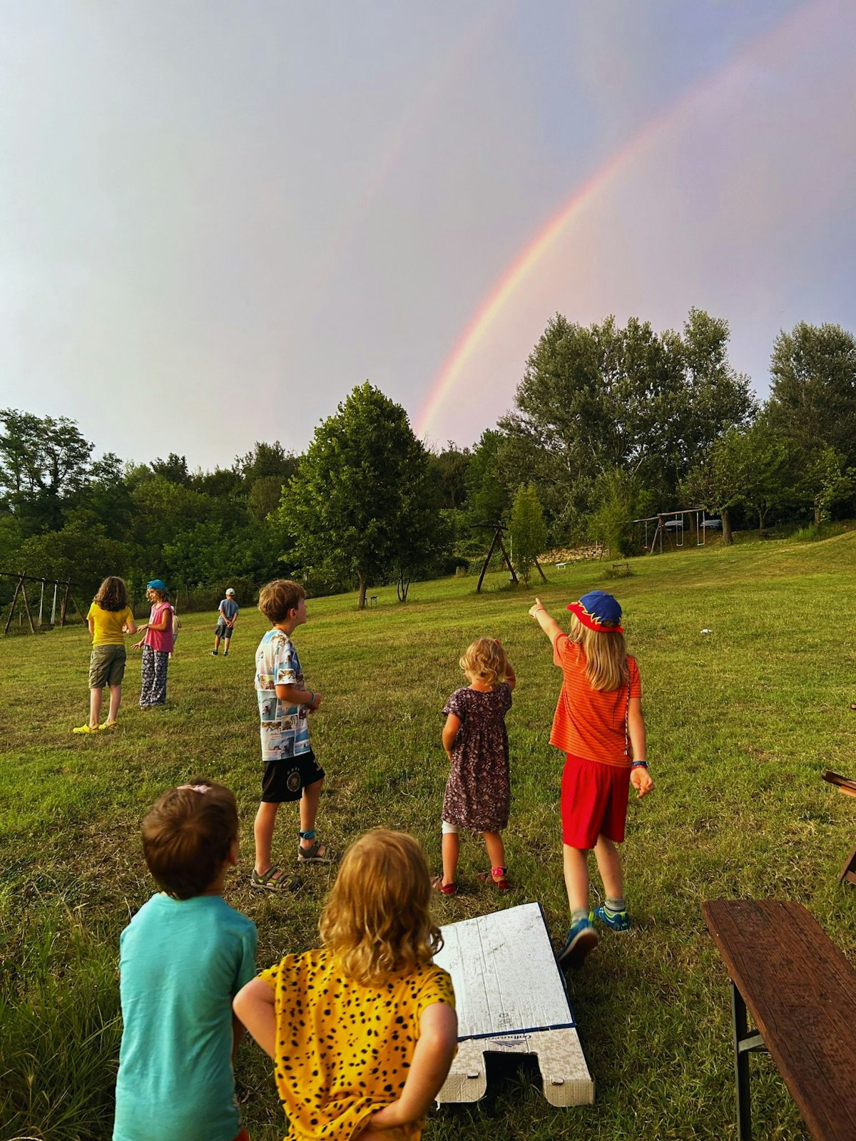 Kinder auf Wiese sehen einen Regenbogen