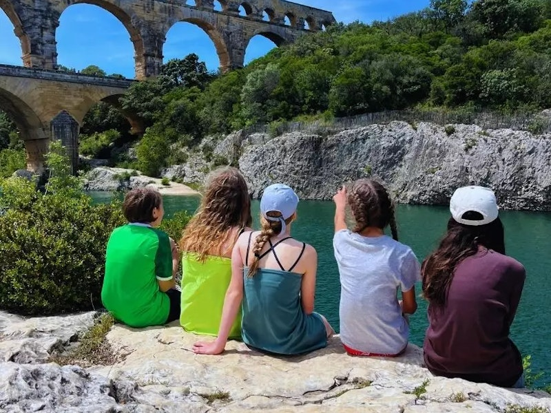Kinder von hinten auf einem Stein an einem See