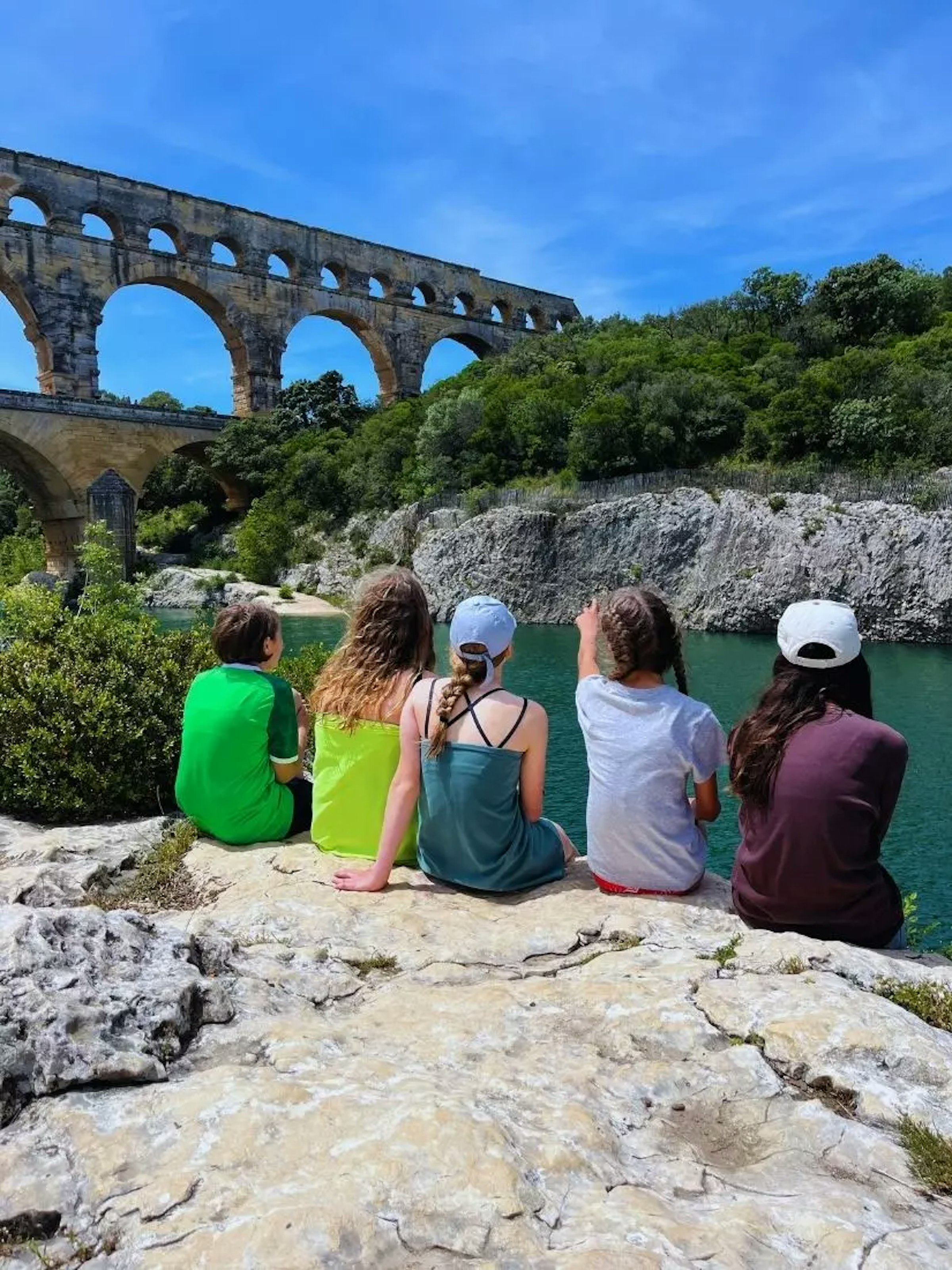 Kinder von hinten auf einem Stein an einem See