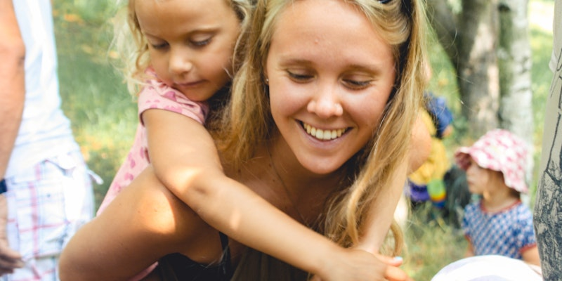 Eine junge Frau die ein Mädchen auf dem Rücken trägt