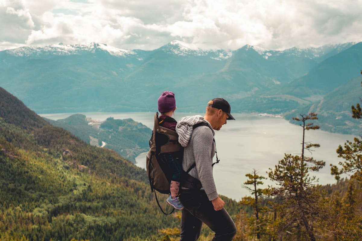 Ein junger Mann der ein Kind auf dem Rücken trägt vor einer Bergkulisse