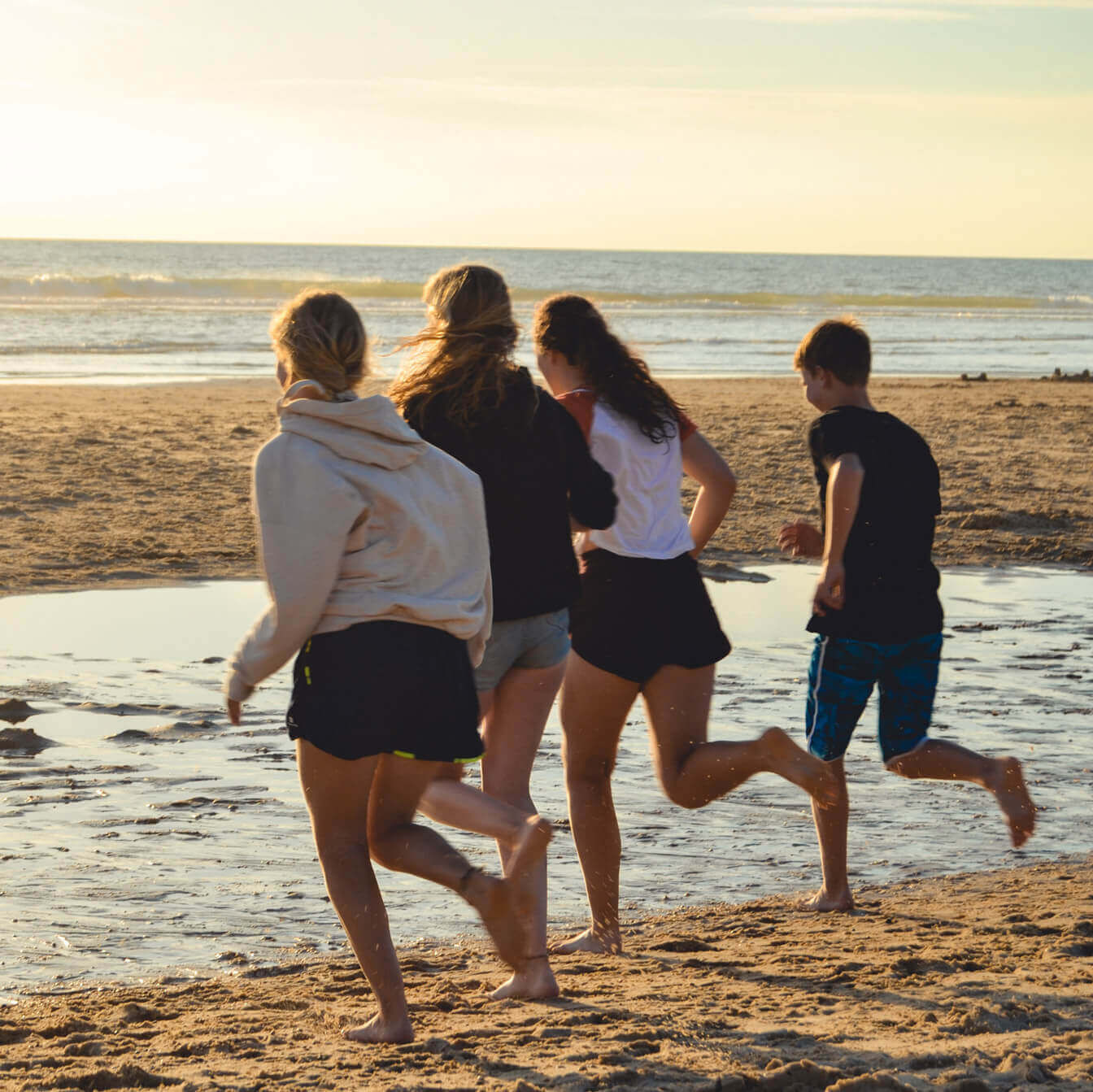Während des Sonnenuntergangs rennen fünf Jugendliche über den Strand in Richtung des Meeres.
