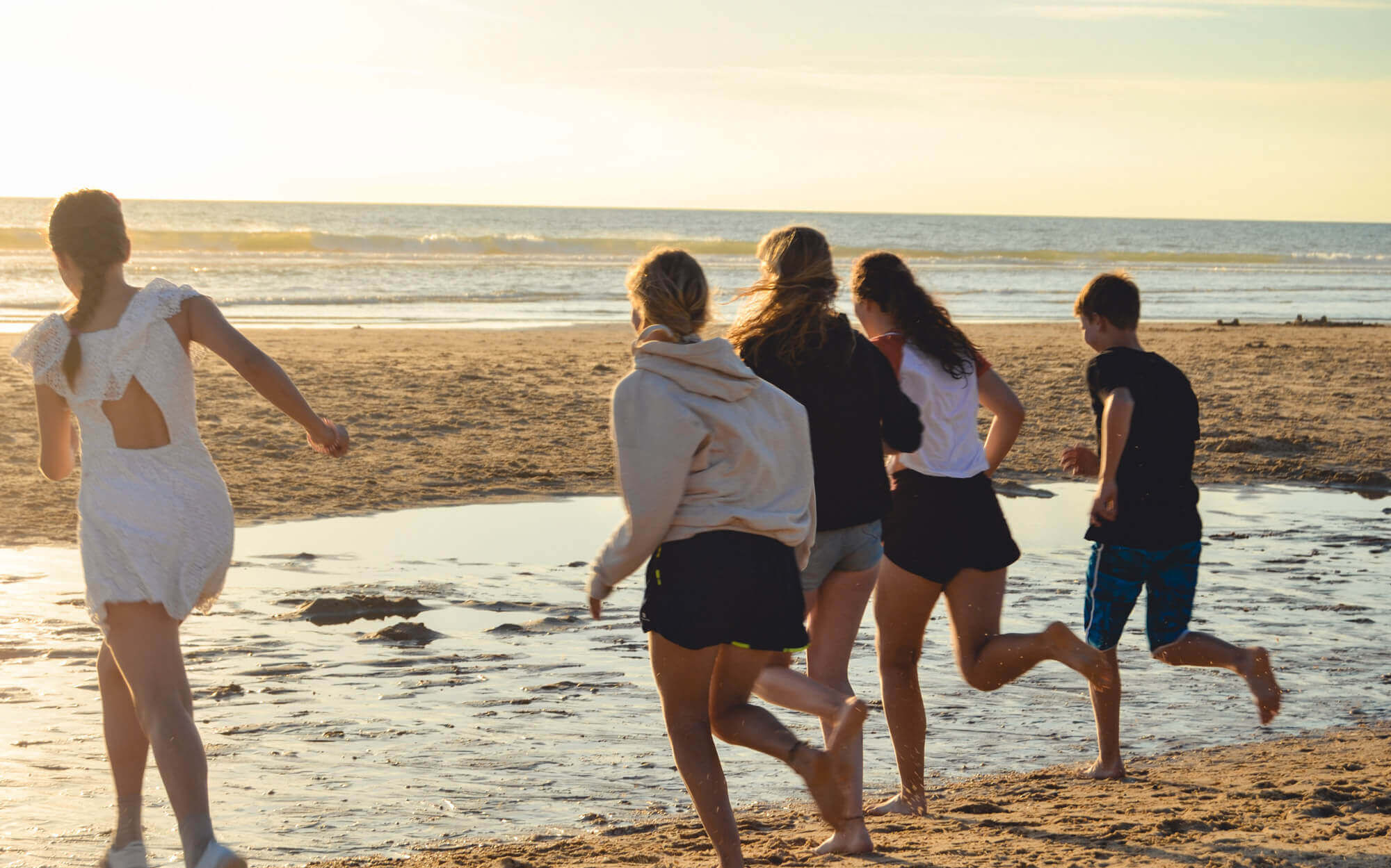 Während des Sonnenuntergangs rennen fünf Jugendliche über den Strand in Richtung des Meeres.
