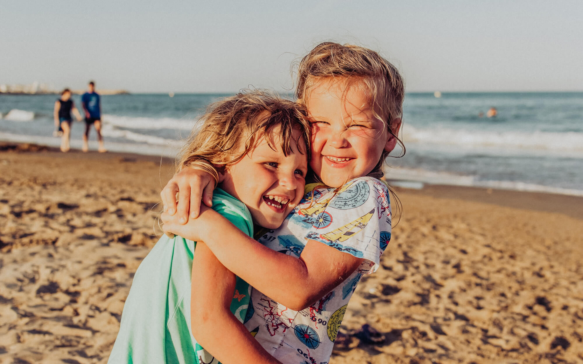 Zwei junge Mädchen am Strand liegen sich lachend in den Armen