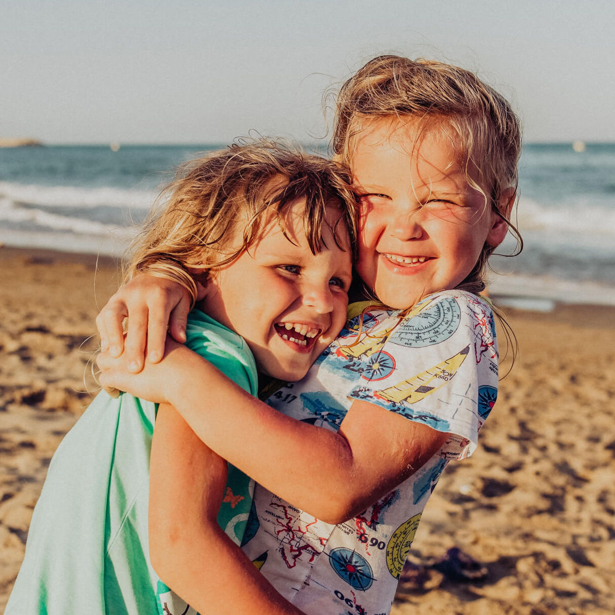 Zwei junge Mädchen am Strand liegen sich lachend in den Armen